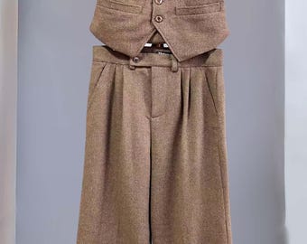 May include: A brown herringbone waistcoat and matching trousers set. The waistcoat features a V-neckline, five front buttons, and two welt pockets. The trousers have a pleated front, a buttoned waistband, and wide legs with cuffed hems. A label reading Vintage is visible.