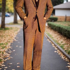 May include: A brown tweed suit with a matching blazer and trousers. The suit features a notched lapel, a two-button closure, and pockets. The person is wearing a brown vest, a yellow tie, and brown leather shoes. The suit is worn on a paved walkway.