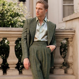 Könnte beinhalten: Ein zweireihiger olivgrüner Blazer mit Fischgrätenmuster und dazu passender Hose mit hoher Taille, kombiniert mit einem hellen, salbeigrünen Satinhemd. Der Blazer hat breite Revers und dunkle Knöpfe, die Hose ist vorne gefaltet.