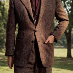 May include: A brown herringbone tweed suit with a matching vest, blue shirt, and burgundy tie. The suit has a classic two-button closure and a pocket square. The outfit is suitable for formal occasions.