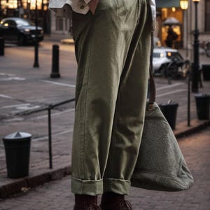 Puede incluir: Pantalones de talle alto en color verde oliva con detalle de hebilla lateral y bajos vueltos, combinados con una chaqueta blanca, botas de cuero marr&oacute;n oscuro con cordones y un bolso grande verde oliva con un sutil patr&oacute;n en relieve.