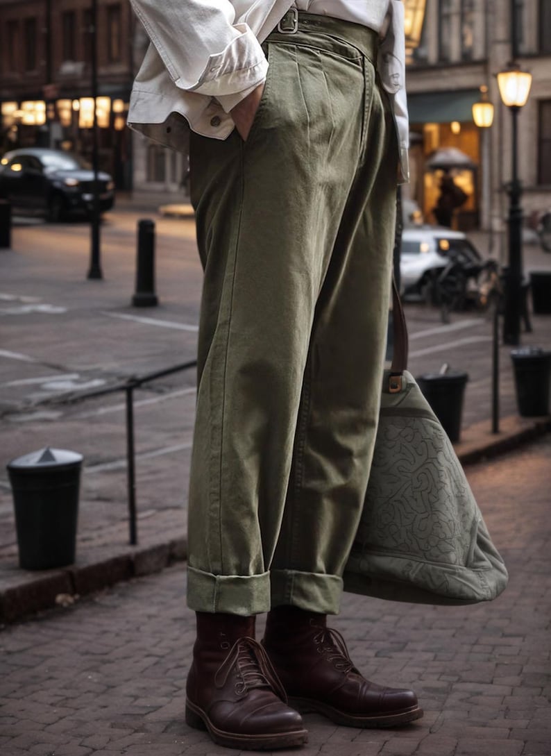 Puede incluir: Pantalones de talle alto en color verde oliva con detalle de hebilla lateral y bajos vueltos, combinados con una chaqueta blanca, botas de cuero marr&oacute;n oscuro con cordones y un bolso grande verde oliva con un sutil patr&oacute;n en relieve.