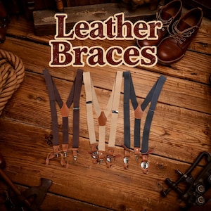 Puede incluir: Cuatro pares de tirantes de cuero en marrón, beige y azul marino se muestran sobre una superficie de madera. Los tirantes tienen detalles de cuero y cierres metálicos. El texto "Leather Braces" está en la parte superior de la imagen.