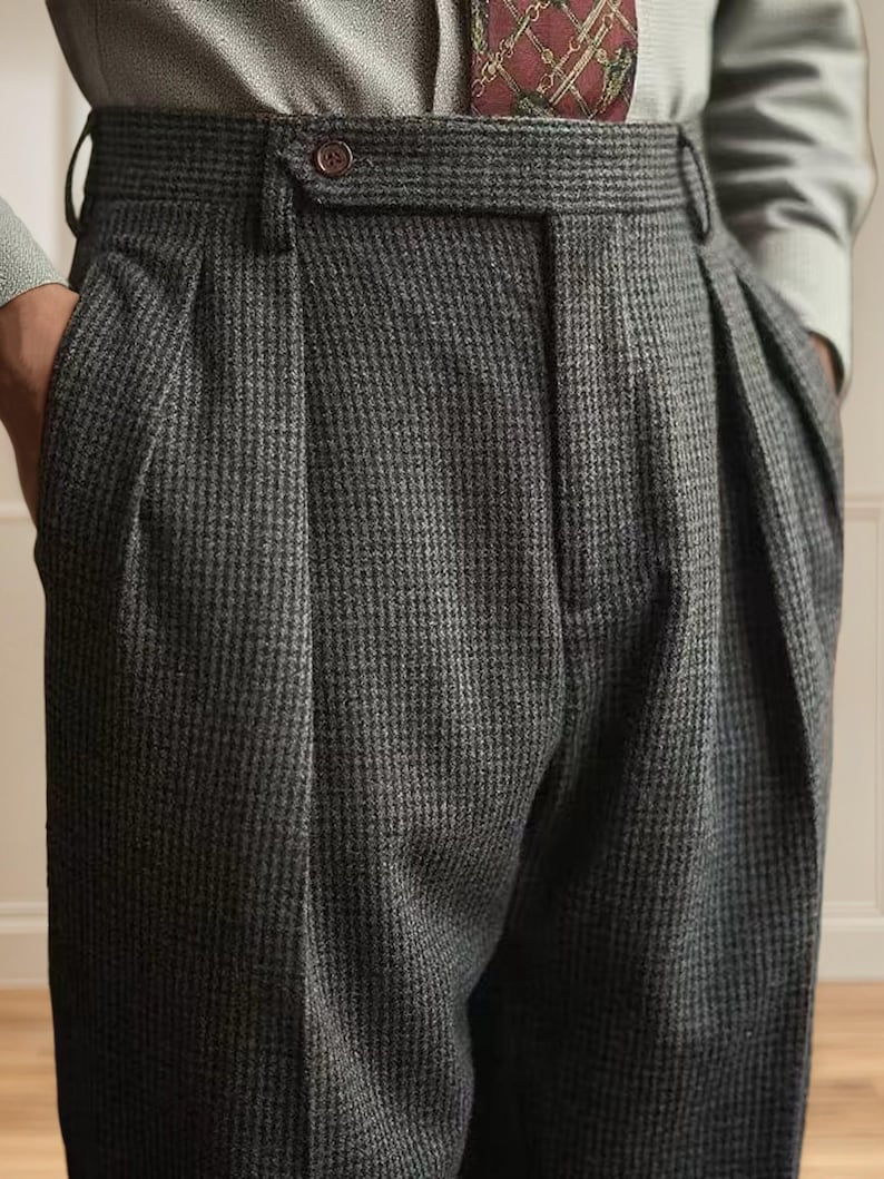 K&ouml;nnte beinhalten: Nahaufnahme einer grauen Hose mit Hahnentrittmuster und Falten. Die Hose hat einen Knopfverschluss und G&uuml;rtelschlaufen. Der Stoff scheint eine Wollmischung zu sein. Die Hose ist Teil einer klassischen Herrenkollektion.