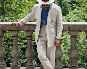 May include: A beige double-breasted linen suit jacket and matching high-waisted trousers, paired with a blue collared shirt, a cream-colored fedora hat with a dark brown band, and light beige loafers, creating a coordinated ensemble.