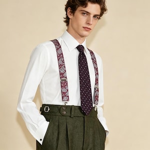 May include: A white dress shirt paired with a dark green pair of trousers. The outfit is accessorized with a burgundy tie with white polka dots and matching paisley suspenders. The ensemble is completed with a belt and a pair of cufflinks.
