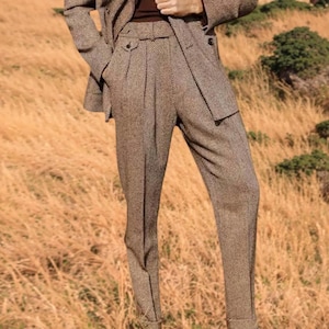 May include: A brown herringbone suit, including a blazer and tailored trousers. The trousers have a high waist and pleats. The suit is made of a textured fabric and is suitable for business or formal wear.