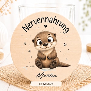 Könnte beinhalten: Ein runder Holzuntersetzer mit einer Illustration eines sitzenden braunen Otters. Der Text "Nervennahrung" ist schwarz über dem Otter gedruckt, und der Name "Martin" steht darunter. Der Text "13 Motive" befindet sich am unteren Rand.