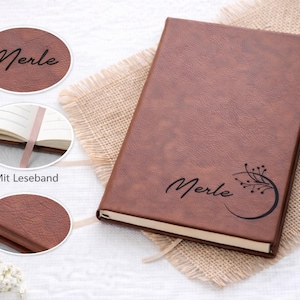 Könnte beinhalten: Ein braunes Lederjournal mit dem Namen "Merle" in Schreibschrift und einem floralen Design. Das Journal hat ein Leseband und wird auf einem Jutegewebe präsentiert.