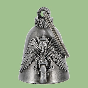 May include: A silver-colored motorcycle bell with a detailed design. The bell features a skeleton with wings, a crown, and a motorcycle. The bell has a loop at the top for hanging.