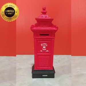 Puede incluir: Un buzón decorativo rojo con un diseño detallado, con una ranura para cartas y una pequeña puerta. El buzón está montado sobre una base negra con el número "5/8000" impreso. Una pegatina dorada con el texto "BEST QUALITY LIMITED EDITION GUARANTEED" está en la esquina superior izquierda.