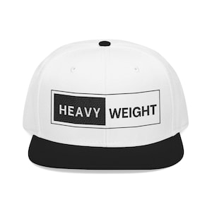 May include: A white baseball cap with a black peak. The front of the cap features a rectangular design with the words "HEAVY WEIGHT" in black and white.