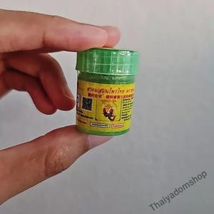 Könnte beinhalten: Ein kleines Glas mit grünem Deckel und gelbem Etikett, gehalten in einer Hand. Das Etikett enthält Text in einer Fremdsprache und einen QR-Code. Der Inhalt des Glases ist nicht sichtbar.