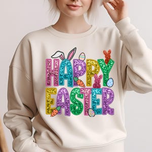 May include: A cream-colored sweatshirt with a glittery "Happy Easter" design. The design features colorful letters, bunnies, eggs, and carrots.