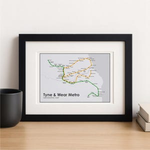 May include: A framed map of the Tyne & Wear Metro system, with green and yellow lines indicating the metro routes. The map has a light grey background, with station names. The black frame surrounds the map, and the text "Tyne & Wear Metro" is visible.