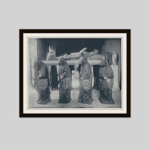 May include: A framed black and white photograph of a tomb scene. Several figures in hooded robes stand before a stone effigy of a person lying down. The figures have shields with heraldic designs.