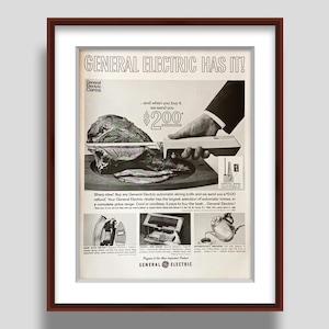 May include: Vintage General Electric advertisement framed in a brown wooden frame. The black and white ad features a hand slicing meat with an electric knife. Text reads "GENERAL ELECTRIC HAS IT!" and "$200".