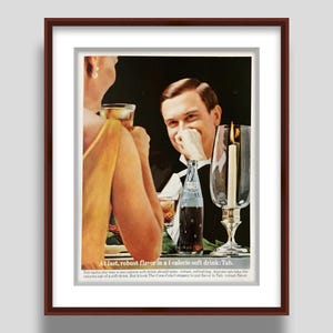 May include: Vintage advertisement framed in a brown wooden frame. The ad features a man and woman at a table with a bottle of Tab soda. Text reads "At last, robust flavor in a 1 calorie soft drink: Tab."