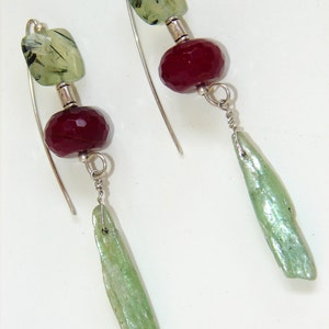 May include: A pair of silver earrings with green and red gemstone beads. The earrings feature a long, thin, green gemstone dangle.