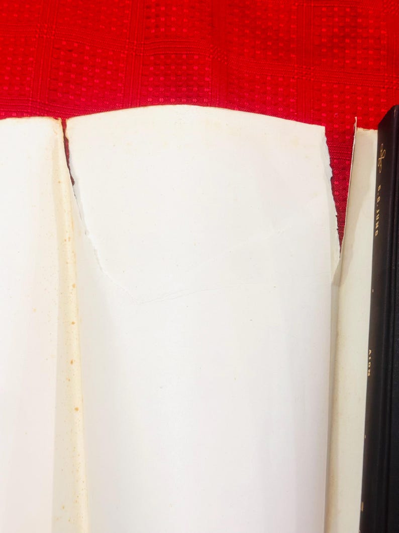 May include: A close-up of a book with white pages and a black spine. The pages are torn and show signs of age. The background is a red, textured surface.