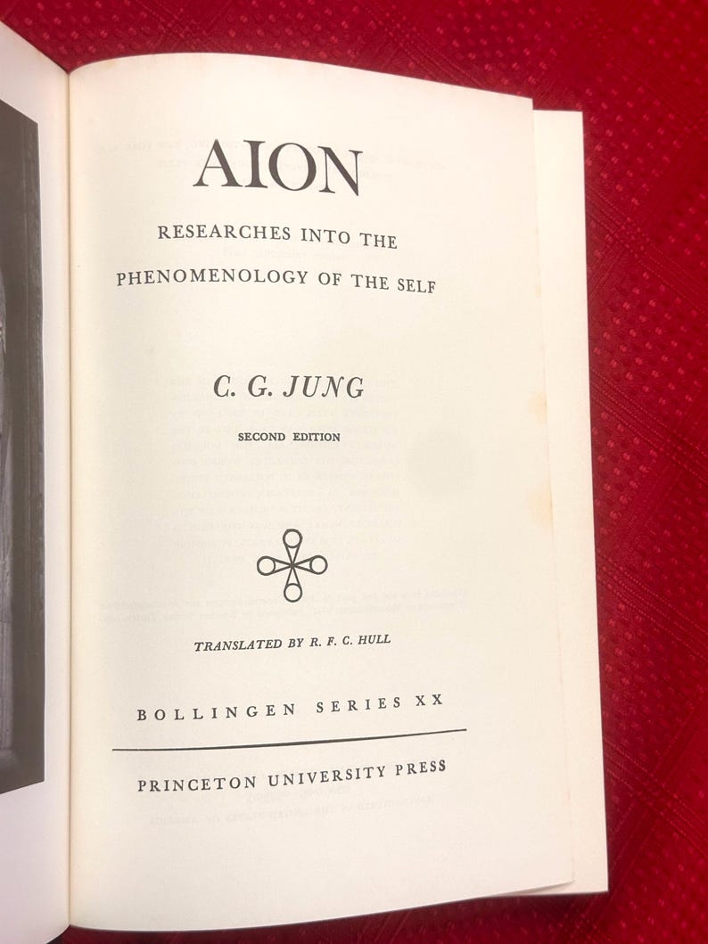 May include: Open book with the title "AION" and the subtitle "Researches Into The Phenomenology Of The Self." The author is C.G. Jung. The book is a second edition, translated by R.F.C. Hull, and published by Princeton University Press.