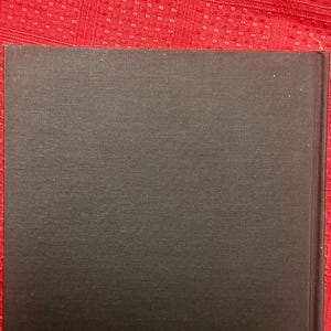 May include: A close-up of a book's spine and cover. The cover is a dark gray color with a textured surface. The book's spine is on the right side of the image.