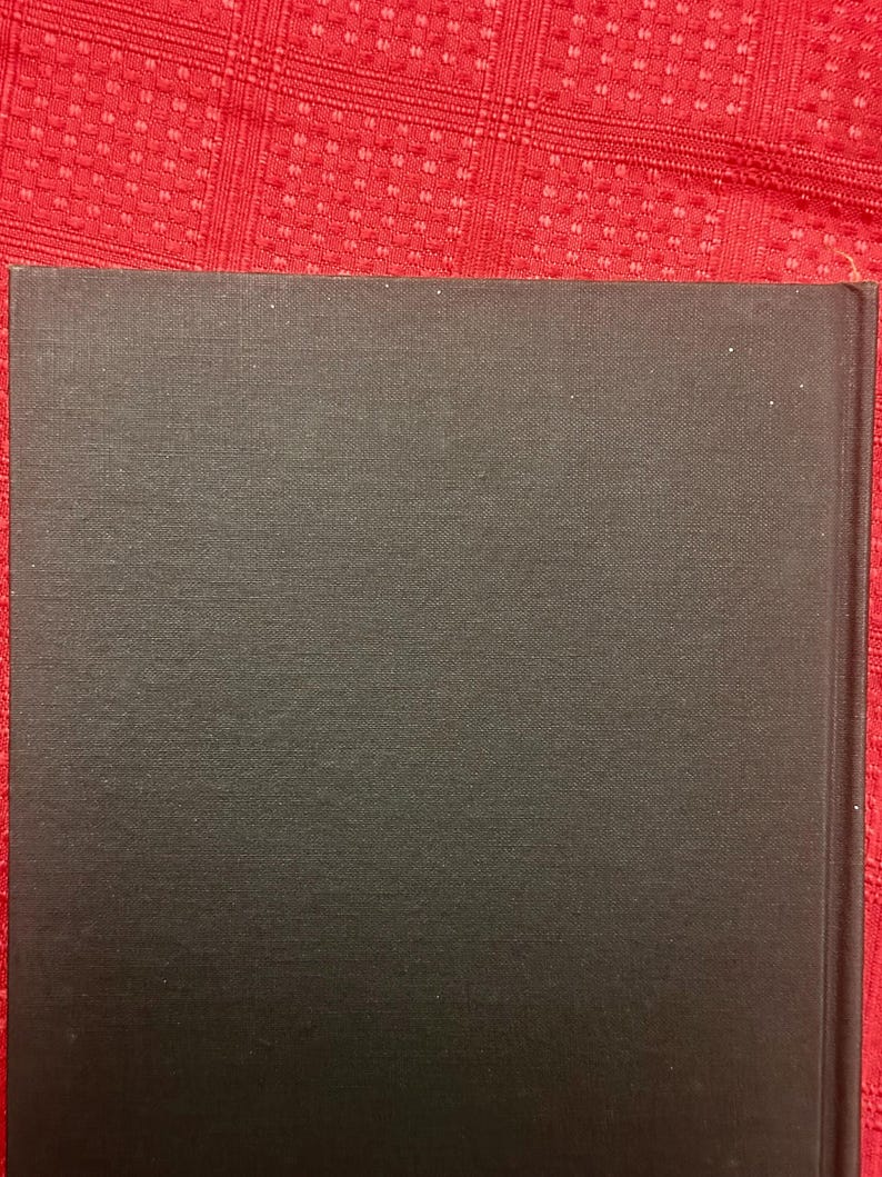 May include: A close-up of a book's spine and cover. The cover is a dark gray color with a textured surface. The book's spine is on the right side of the image.