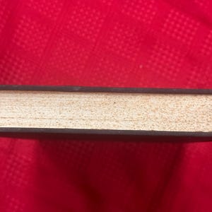 May include: A closed book with a dark brown cover and aged, off-white pages. The book's spine is visible, and the pages have a textured appearance. The book is set against a red background.
