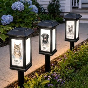 May include: Three black solar-powered garden lanterns with square tops and stakes. Each lantern features a white panel displaying a pet portrait, a name, and dates. The first shows a cat named MILO 2013-2024, the second a dog named MAX 2012-2025, and the third a dog named BUDDY 2011-2024.
