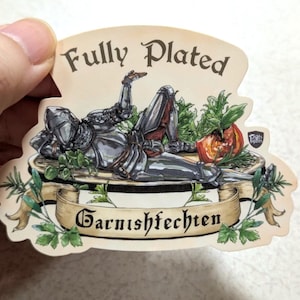 May include: A sticker with a knight in shining armor reclining on a bed of herbs and a tomato. The sticker has the words "Fully Plated" and "Garnishfechten" in a decorative font. The sticker is held by a hand.
