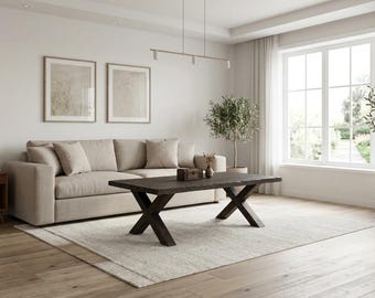 Puede incluir: Una mesa de centro rectangular con acabado de veta de madera marrón oscuro y una base robusta en forma de X. La mesa presenta una superficie gruesa y sólida con un borde natural, situada frente a un sofá beige sobre una alfombra clara en una habitación luminosa.