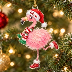 May include: A clear acrylic Christmas ornament shaped like a pink flamingo wearing a red Santa hat with the name Olivia printed on the brim, a red and green patterned scarf, and red glittery boots with white fur trim, hanging by a gold cord.