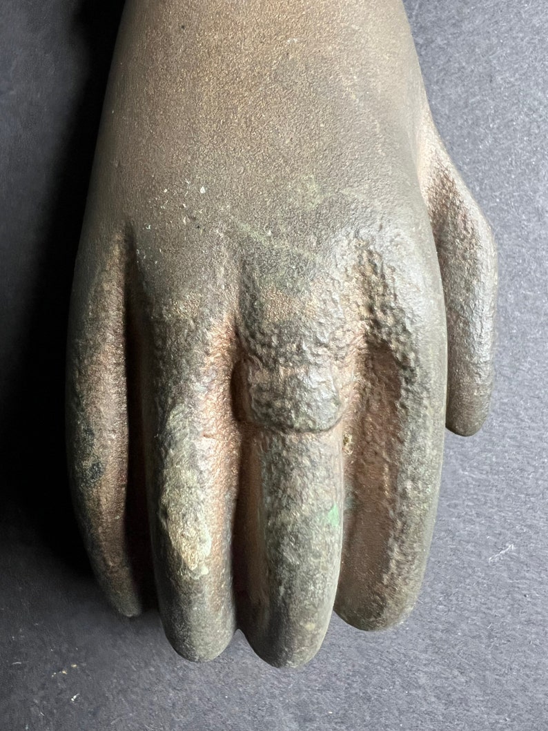 May include: A close-up of a cast iron hand door knocker. The knocker is a realistic depiction of a hand with a ring on the index finger. The hand is a dark brown color with a green patina.