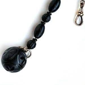 May include: A black beaded chain with a carved black ball charm and a silver clasp.