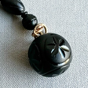 May include: A black carved jet bead necklace with a gold clasp and a large, round, carved jet bead pendant.