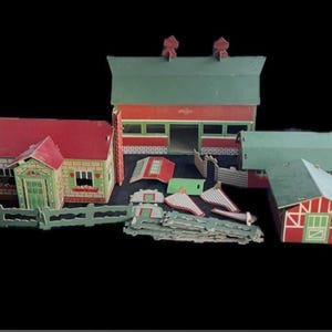 Könnte beinhalten: Ein Vintage-Bauernhof-Spielset mit roter und grüner Farbgebung. Das Set enthält ein Haus, eine Scheune und andere landwirtschaftliche Gebäude sowie Zäune und anderes Zubehör. Die Gebäude haben rote Dächer und grüne Verzierungen. Das Set ist wahrscheinlich aus Pappe oder einem ähnlichen Material.