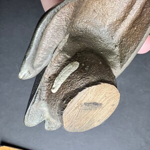 May include: A brown ceramic hand sculpture with a wooden base. The hand is open and the fingers are slightly curled. The base is round and has a wood grain pattern.