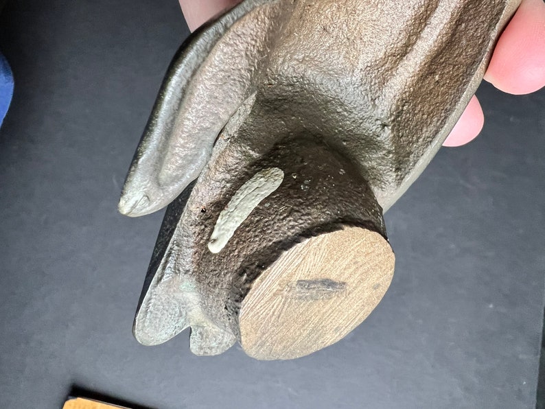 May include: A brown ceramic hand sculpture with a wooden base. The hand is open and the fingers are slightly curled. The base is round and has a wood grain pattern.