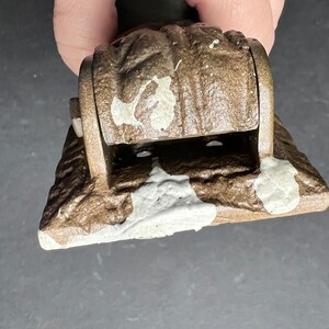 May include: A brown metal hinge with a white paint splatter design. The hinge has a rounded top and a rectangular base.