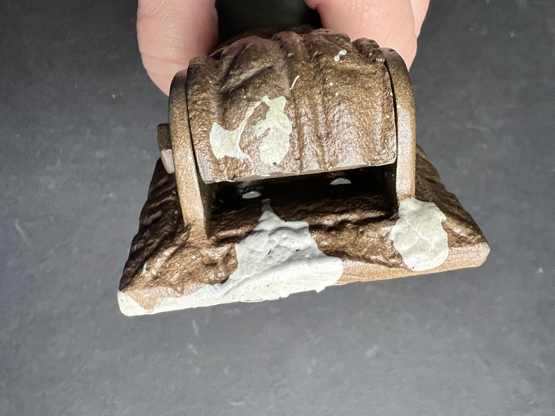 May include: A brown metal hinge with a white paint splatter design. The hinge has a rounded top and a rectangular base.