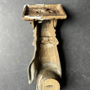 May include: A vintage brass door knocker shaped like a hand. The knocker has a wooden base and a metal hand with a hinged arm.