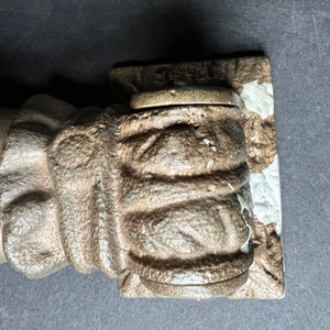 May include: A close-up of a cast iron hand sculpture with a textured surface. The hand is holding a round, metal object.