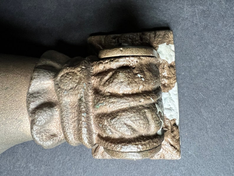 May include: A close-up of a cast iron hand sculpture with a textured surface. The hand is holding a round, metal object.