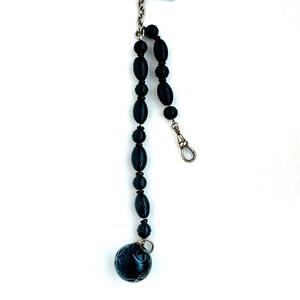 May include: A black beaded watch chain with a carved ball at the end. The chain is attached to a silver T-bar.