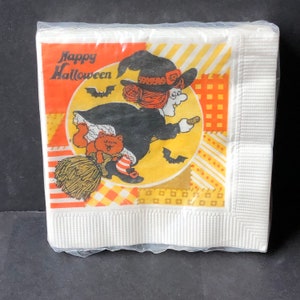 May include: A white paper napkin with a colorful illustration of a witch flying on a broomstick with a cat. The text "Happy Halloween" is printed in orange and black.