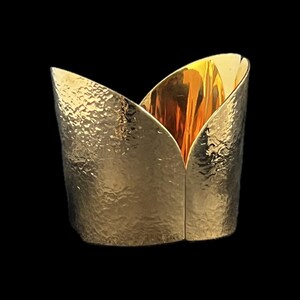 May include: A gold-colored, tulip-shaped container with a hammered texture. The interior has a shiny, reflective gold surface. The container is set against a black background, highlighting its metallic sheen.