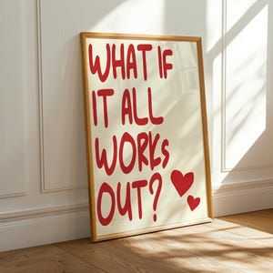 Könnte beinhalten: Ein gerahmter Kunstdruck mit dem Text "WHAT IF IT ALL WORKS OUT?" in Rot, zusammen mit zwei roten Herzen. Das Kunstwerk hat einen cremefarbenen Hintergrund und einen Holzrahmen. Der Druck lehnt an einer weißen Wand.