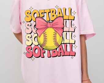 May include: Pink t-shirt with a softball graphic and the text "Softball" repeated three times. The softball is yellow with red stitching and a pink bow.