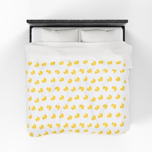 Puede incluir: Una funda nórdica blanca con un estampado repetido de patitos de goma amarillos. La ropa de cama está sobre una estructura de cama negra con almohadas blancas y una sábana superior blanca. Los patos miran en diferentes direcciones.