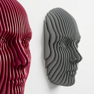 May include: Two wall-mounted sculptures shaped like human faces, constructed from stacked, layered slices. One sculpture is deep red, and the other is matte gray. Both pieces feature a profile view with distinct, parallel horizontal ridges.